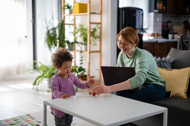 妈妈在笔记本电脑上工作，而她可爱的小女儿正在玩一个教育说教玩具图片下载