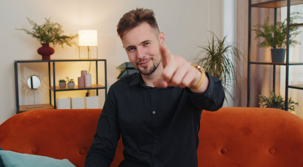 年轻的大胡子男子微笑着，指着相机，选择幸运的赢家，表示，邀请，批准图片下载