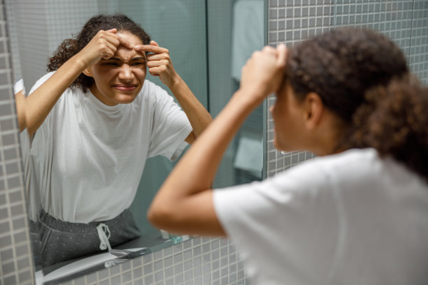 心烦意乱的年轻非洲妇女去除丘疹从她的脸上，而看着镜子在浴室的家图片下载