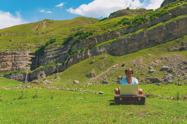 这个女孩在山里用笔记本电脑工作。自由职业图片下载