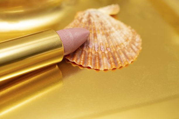 粉红色口红旁边的贝壳，金色背景，软焦点图片下载