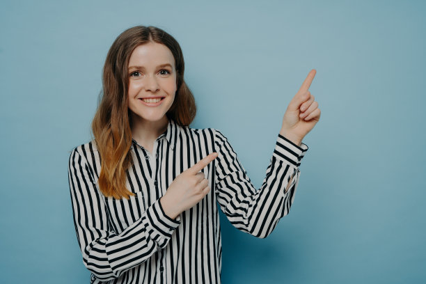 年轻女子微笑着用两根食指向上指，脸上带着快乐的表情图片下载