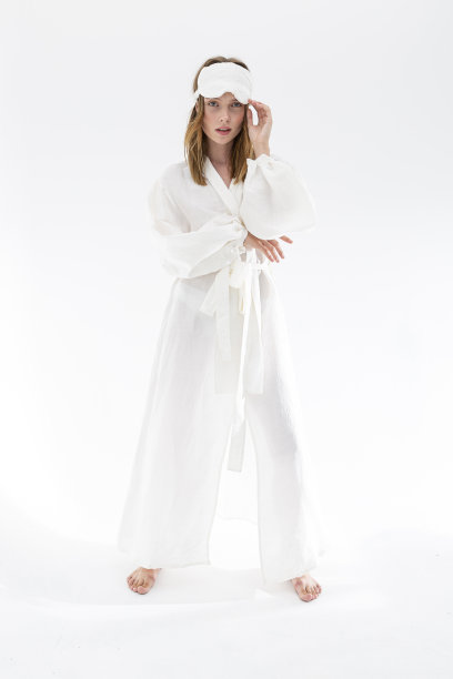 漂亮的年轻女子在丝绸织物白色睡衣和睡眠面具看着相机。图片下载
