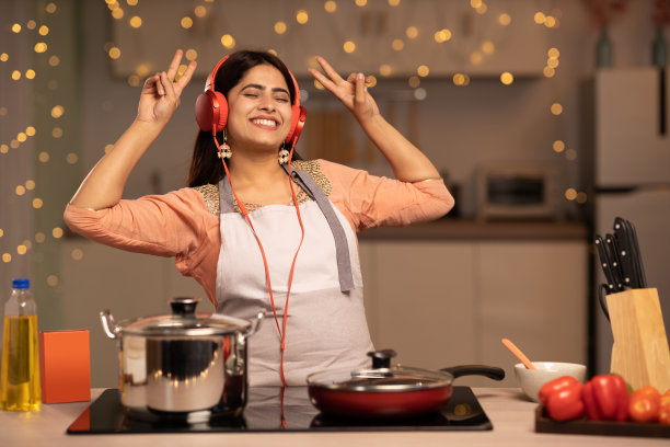 年轻女子在家做饭时听音乐。库存图片图片下载