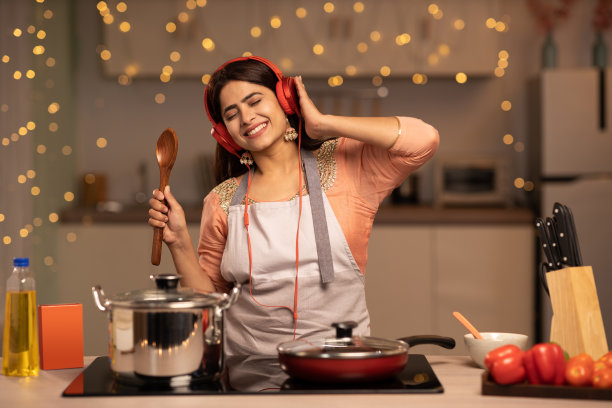 年轻女子在家做饭时听音乐。库存图片图片下载