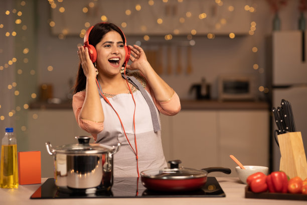 年轻女子在家做饭时听音乐。库存图片图片下载