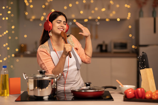 年轻女子在家做饭时听音乐。库存图片图片下载