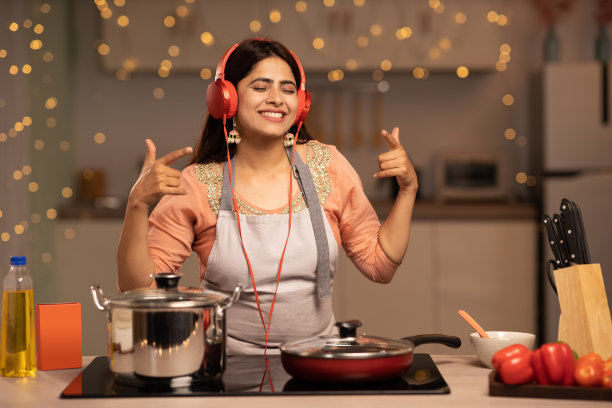 年轻女子在家做饭时听音乐。库存图片图片下载