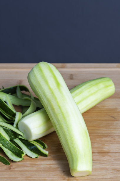 剥了皮的西葫芦和它们的皮条放在厨房木板上。食物制备概念。图片下载