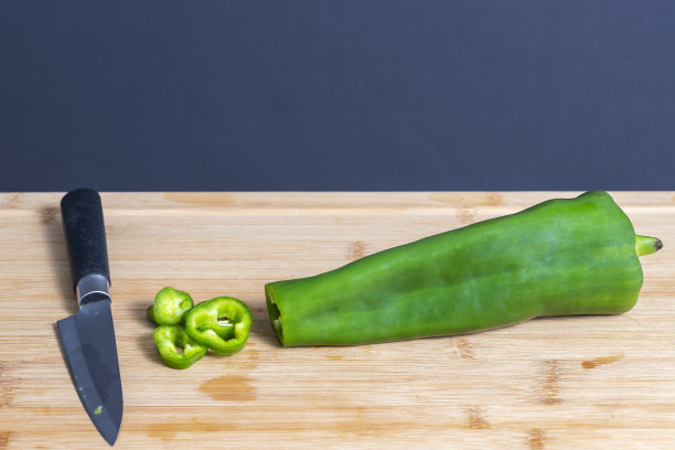 在厨房木板上用刀切一份青椒。食物制备概念。图片下载