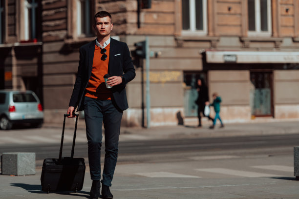 我要去机场航站楼。自信的商务旅行者走在城市的街道上，拉着他的手提箱，喝着咖啡，用智能手机说话图片下载