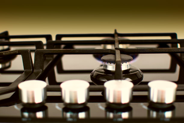 黑色黄色背景上有调节器的煤气灶。燃烧器亮了，选择性聚焦图片下载