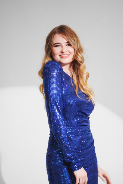 一个美丽苗条的女人，在白色背景上穿着闪亮的蓝色连衣裙。图片下载