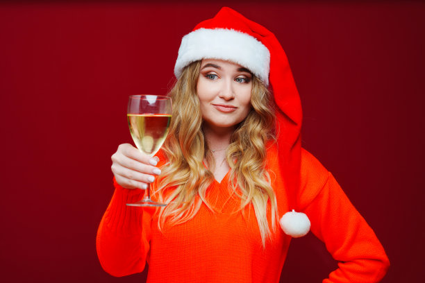 一个美丽的女人戴着圣诞老人的帽子，红色背景上有香槟。图片下载