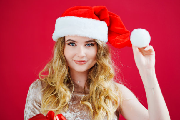 一个红色背景上戴着圣诞老人帽子的美丽女人。图片下载