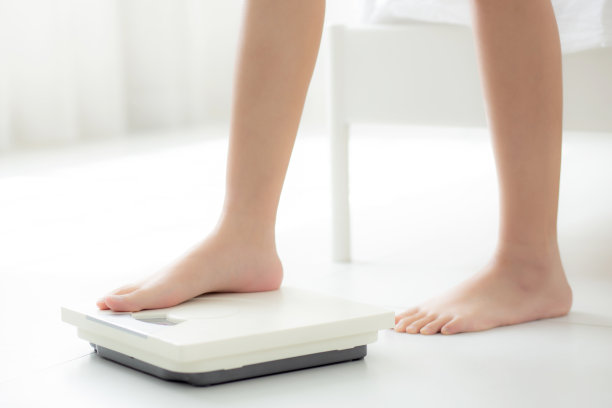 近距离观察站在室内体重秤上的女性，测量超重和节食，健康和减肥，检查脂肪称重，室内，健康的概念。图片下载