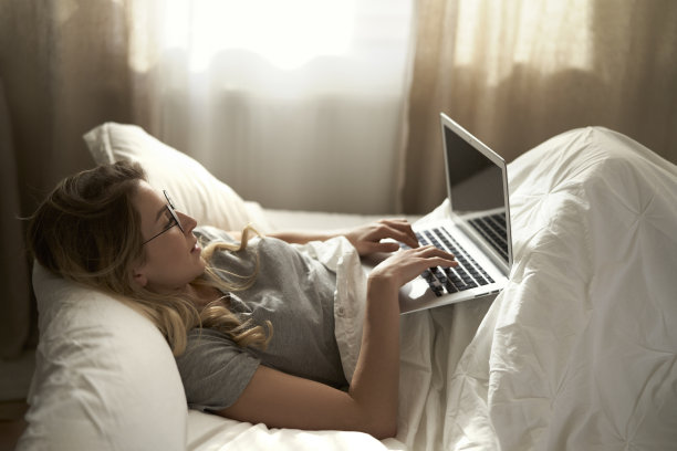 白人妇女使用笔记本电脑，早上躺在家里的床上图片下载