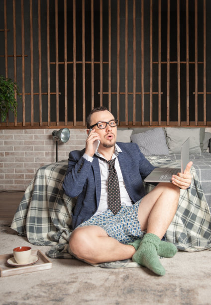 穿着西装和内裤的男人穿着绿色袜子在家工作，坐在卧室的地板上图片下载