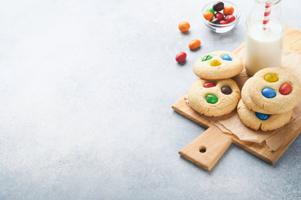 自制饼干配上五颜六色的巧克力糖果和牛奶。在浅灰色的背景上，有一瓶牛奶和一堆彩色的饼干。婴儿食品的概念。副本的空间。图片下载