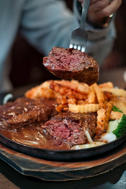 人们在黑色的盘子里用刀叉吃美味的热铁板烧牛排和薯条图片下载