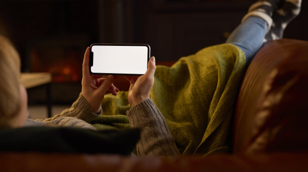 近距离的女人在家里躺在沙发上，舒适的火流到空白屏幕的手机图片下载