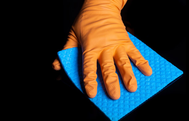 戴着手套的手用蓝色餐巾擦黑桌子。家庭清洁过程的特写镜头。冠状病毒期间的医疗保健和消毒概念图片下载