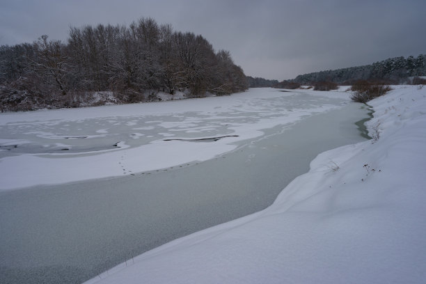 俄罗斯冬季景观在阴天，河流被冰雪覆盖图片下载