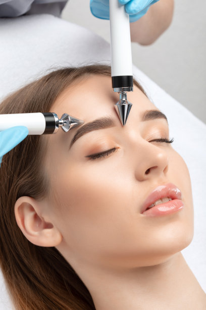 一位美容医生在美容健康沙龙里用设备给一位年轻女性做微电流面部治疗。美容和专业护肤。图片下载