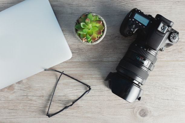 摄影师工作站有相机，笔记本电脑，眼镜放在木桌上图片下载