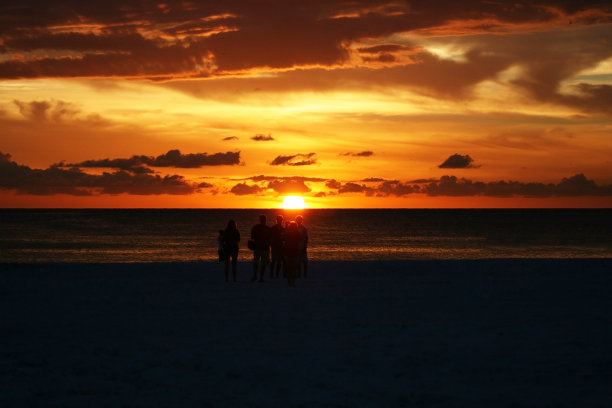 一小群人在海滩上看日落剪影与戏剧性的天空图片下载