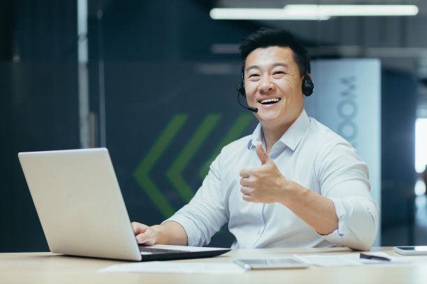 一名年轻的男学生坐在办公室、联合办公空间、图书馆里，用笔记本电脑戴着耳机图片下载