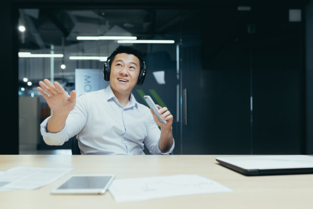 快乐的年轻亚洲商人在工作场所听音乐耳机。拿着电话，唱歌图片下载