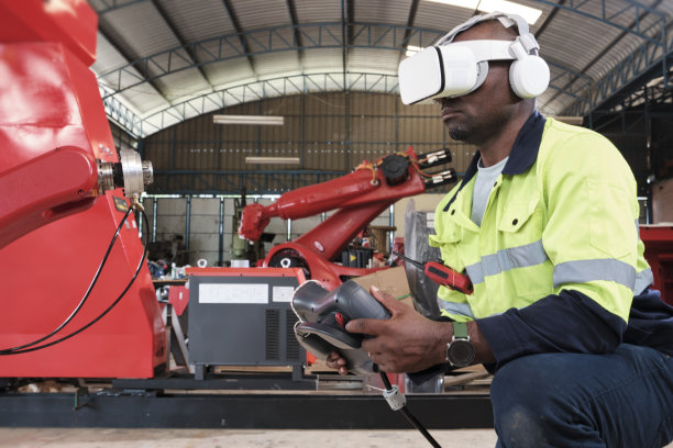 戴着VR眼镜的黑人工程师在制造工厂控制机械臂。图片下载