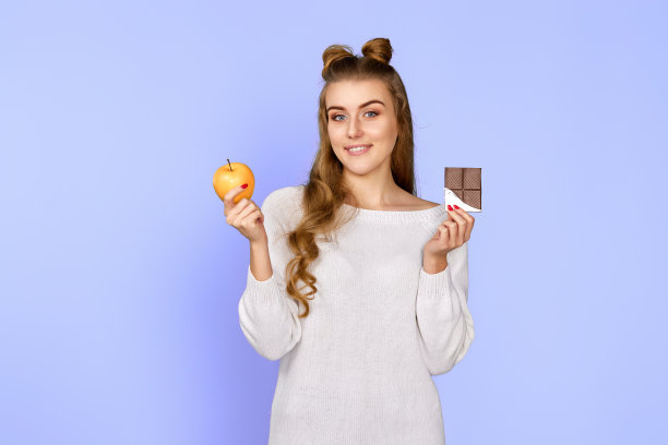 穿着毛衣的女人展示了甜美的巧克力棒和新鲜的苹果图片下载