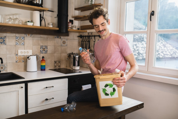 快乐的年轻人把厨房里的塑料瓶放进回收箱图片下载