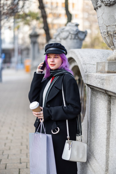 一位美丽的年轻女子走在城市的街道上，喝着咖啡，用着电话。图片下载