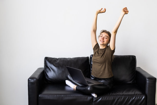 年轻的女商人在家工作，坐在沙发上伸展双臂，开心地微笑着图片下载