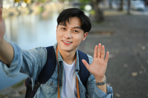 站在泰国北部清迈老城，微笑着挥手的男性旅行博主正在录制视频。图片下载