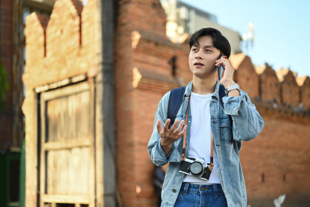 一名年轻男子站在泰国北部清迈的一堵古老的城墙上打电话。图片下载