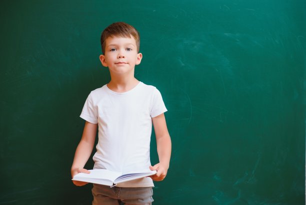 有趣的男孩在教室里的绿色学校董事会附近。小学。回到学校。图片下载