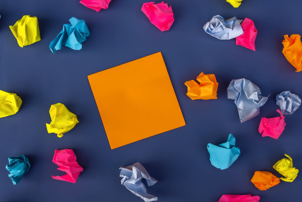 橙色的纸币和许多彩色的皱褶纸球围绕在紫色的背景上。静物，平面设计，俯视。复制文本空间图片下载