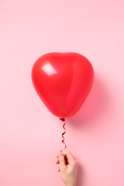 情人节快乐的概念。女性手拿红色心形气球在粉红色的背景。图片下载