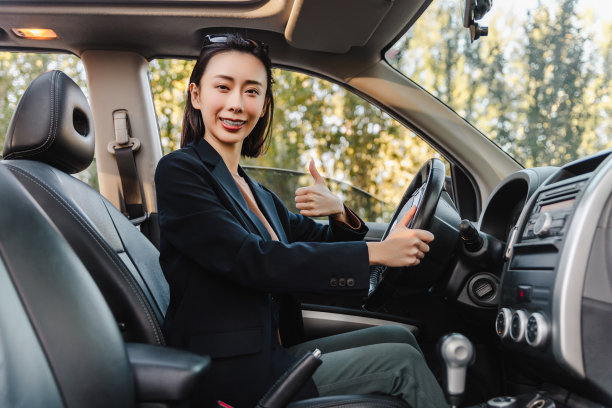 亚洲女人开着车，面带微笑。一个年轻成功快乐的女人正在开车。图片下载