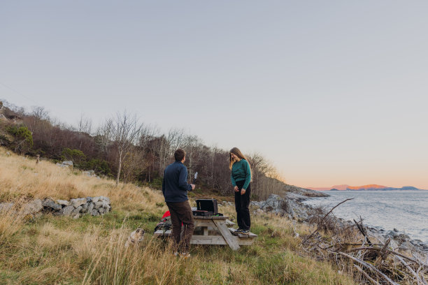 一个女人和一个男人带着一只狗在海边野餐，凝视着快乐的日落时分图片下载