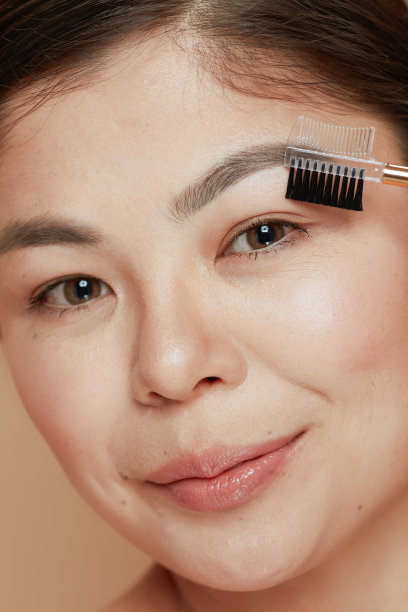 年轻女子的眉毛刷孤立在米色背景图片下载