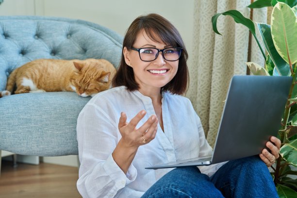 中年妇女使用笔记本电脑，躺在扶手椅上睡觉的猫图片下载