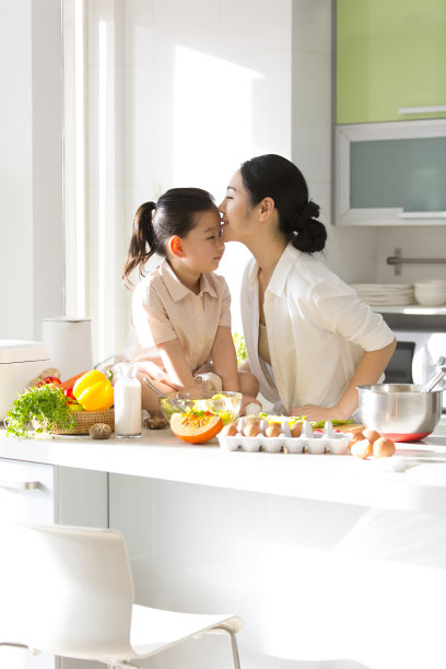 家庭厨房的血统。年轻的母亲带着孩子在厨房里亲吻女儿的额头。- - -库存图片图片下载