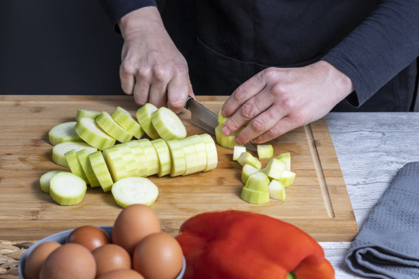 工作妇女在厨房木板上切小胡瓜的手。褪到前面，灰色碗与鸡蛋和红辣椒。食物制备概念。图片下载