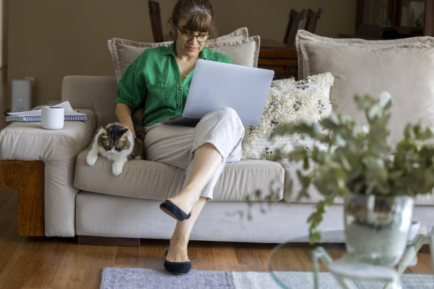 积极的中年妇女在家和她的猫一起使用笔记本电脑。图片下载