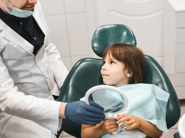 女孩坐在牙科诊所里，对着镜子看她的牙齿图片下载